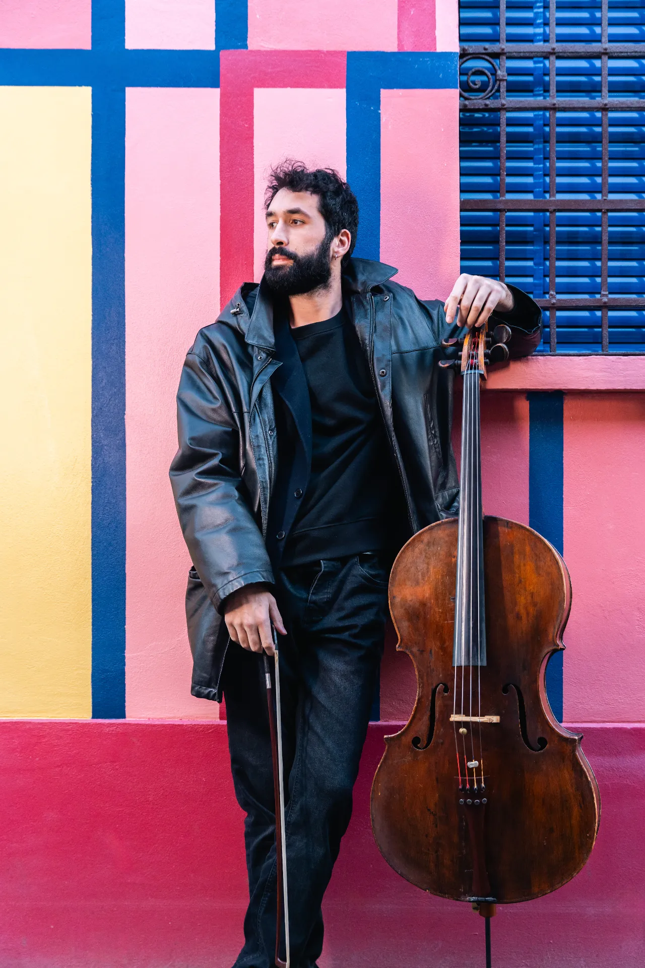 Immagine profilo di Antonio Cortesi appoggiato ad un muro colorato di diversi colori mentre tiene il violoncello